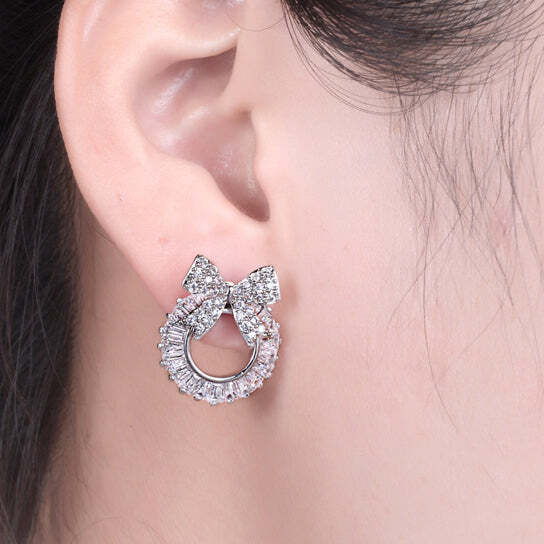 Silver bow-shaped earring worn on an ear with a plain background