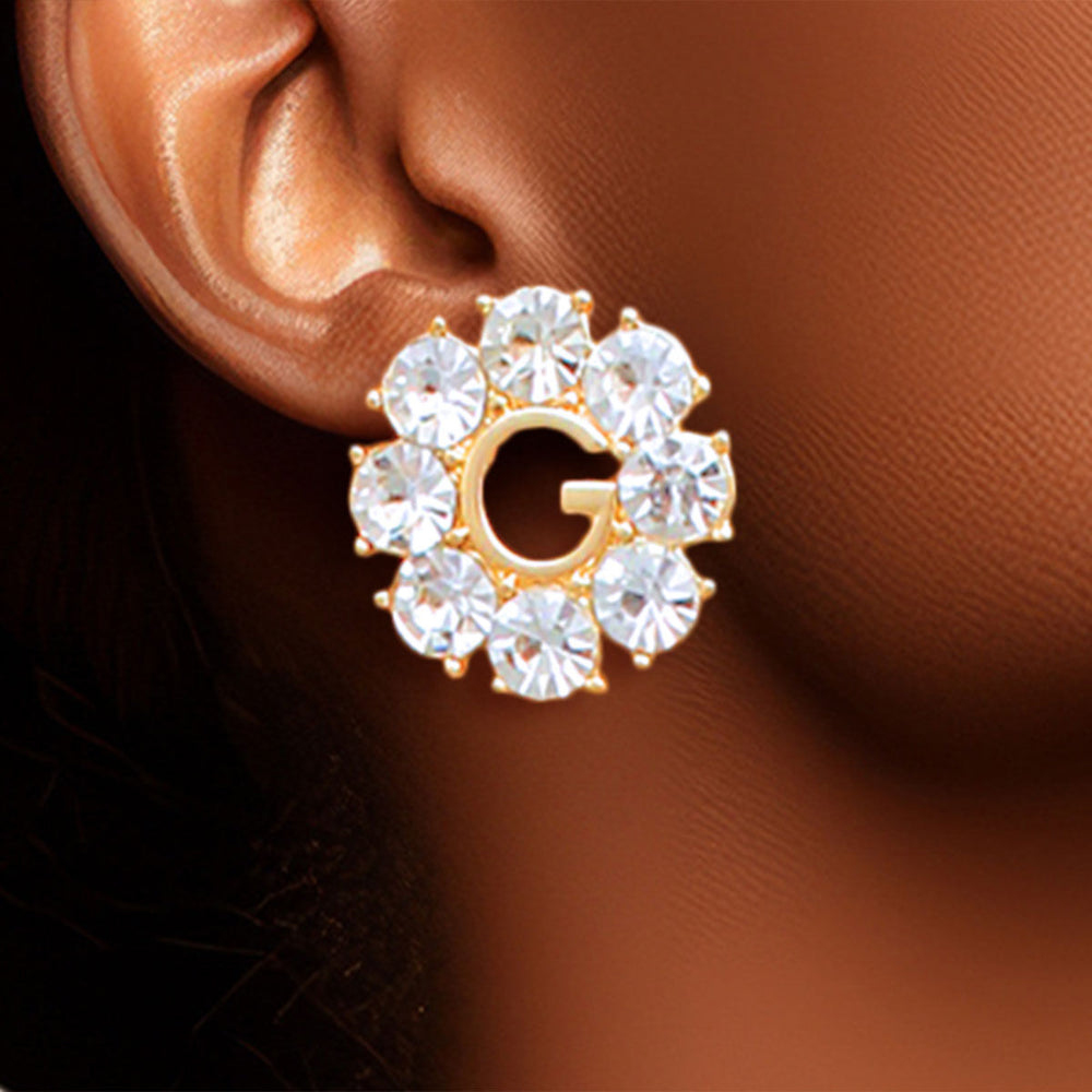Gold earring with clear gemstones worn on an ear against a brown background