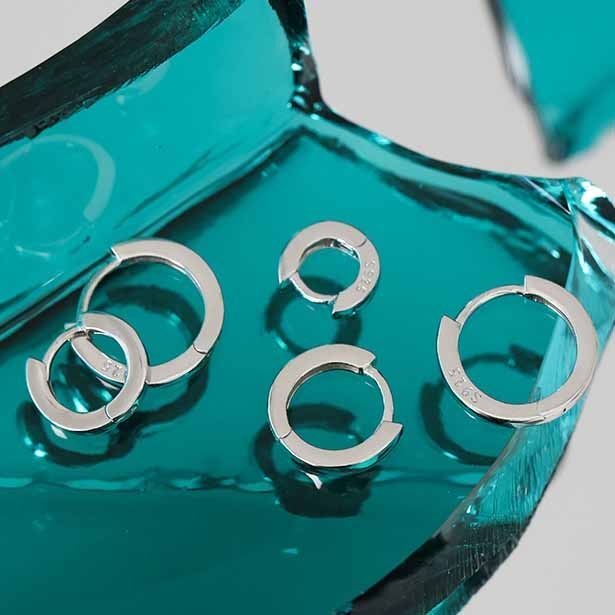 Silver hoop earrings on a teal mirror surface