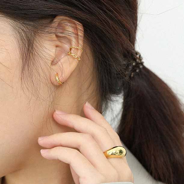 Close-up of a person wearing gold earrings and a ring with a plain background