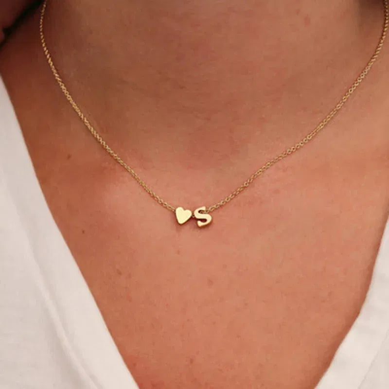 Gold necklace with a heart and 'S' pendant on a person wearing a white top.