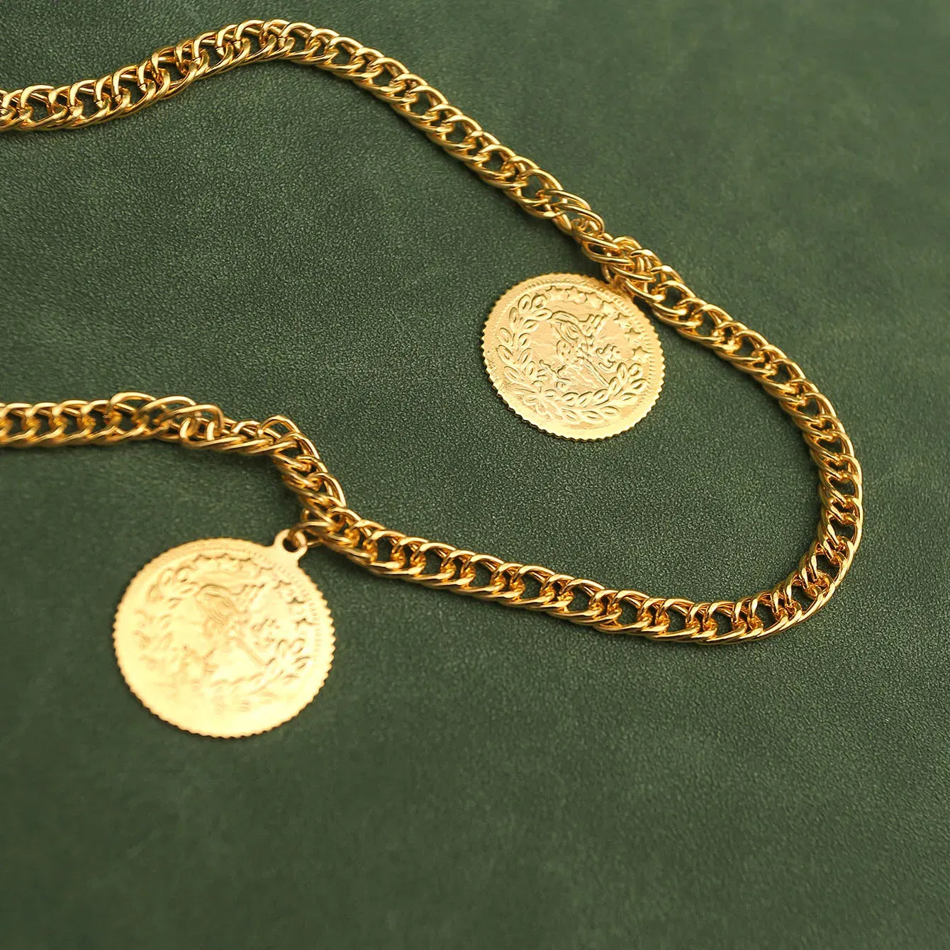 Gold chain necklace with two coins on a green background