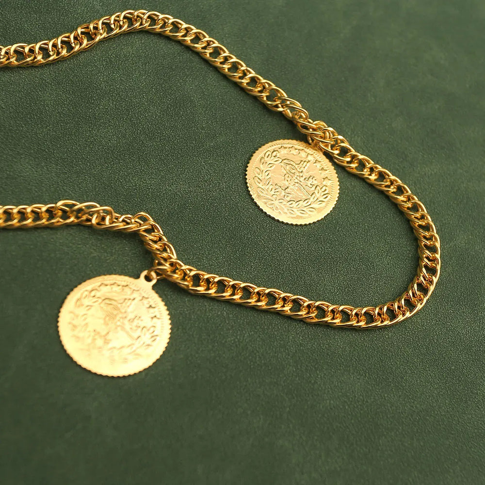 Gold chain necklace with two coins on a green background