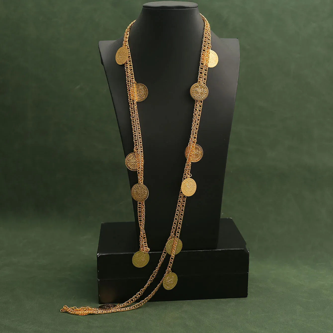 Gold necklace with circular pendants on a black mannequin against a green background